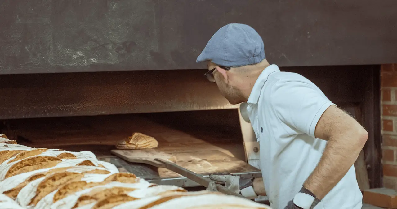 A baker taking fresh bread out of a professional oven